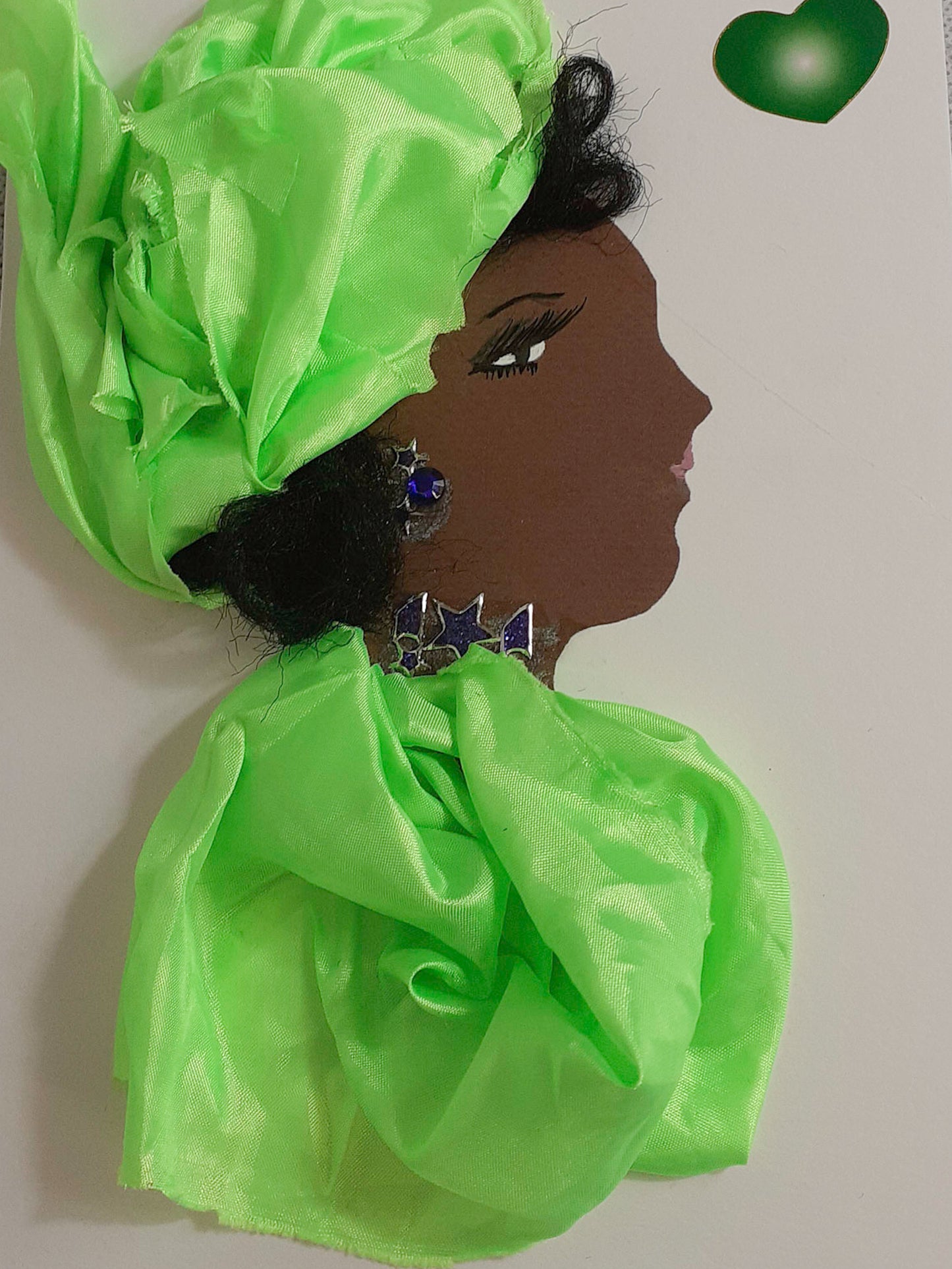 This card is of a woman given the name Lola. Lola wears a matching lime green blouse and headscarf, both a silky material. Her necklace and earrings also match, both are purple glittery stars. In the top right corner, there is a green heart.