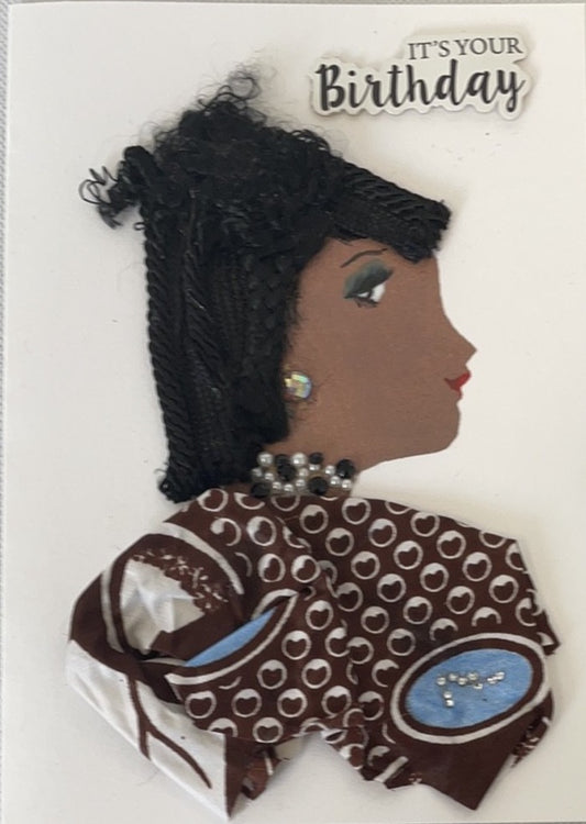 **Naomi Newton**
A handmade card showing a woman with dark skin and textured black hair styled up. She has light green eyeshadow, shiny round earrings, and a pearl necklace. Her dress is brown with white polka dots and blue ovals, decorated with small beads. The card says "It's your Birthday" in raised letters.