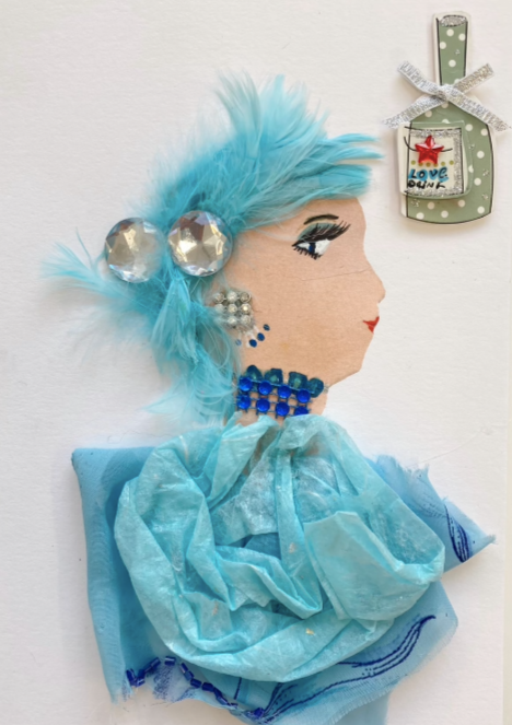 This card has been given the name Talia. She is wearing  a sky blue blouse with gold flecks in it. Her necklace has three separate strands, all that are a royal blue. In her light blue   feathery hair, there are two large diamante gems.  Her earring is made of  small diamontes in the shape of a square. In the top right corner, there is a light green polka-dotted bottle which says "love drink" and has a small silver bow on it.