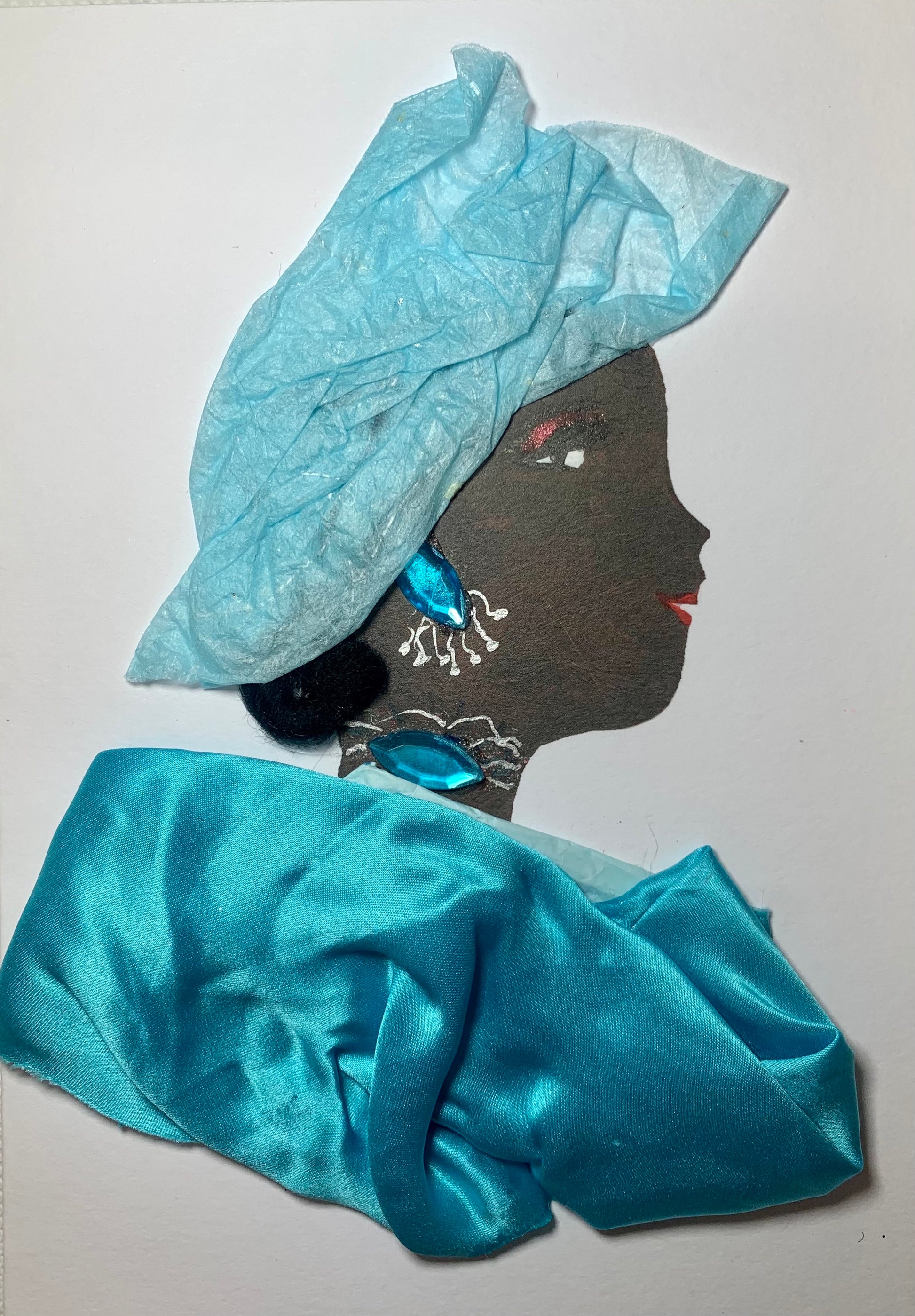 This card has been given the name Dami. Dami wears a billowing sky blue silk blouse. Her jewellery is pointed shape oval gems that are a matching blue to the dress. Her headscarf is a slightly lighter blue recycled paper material.