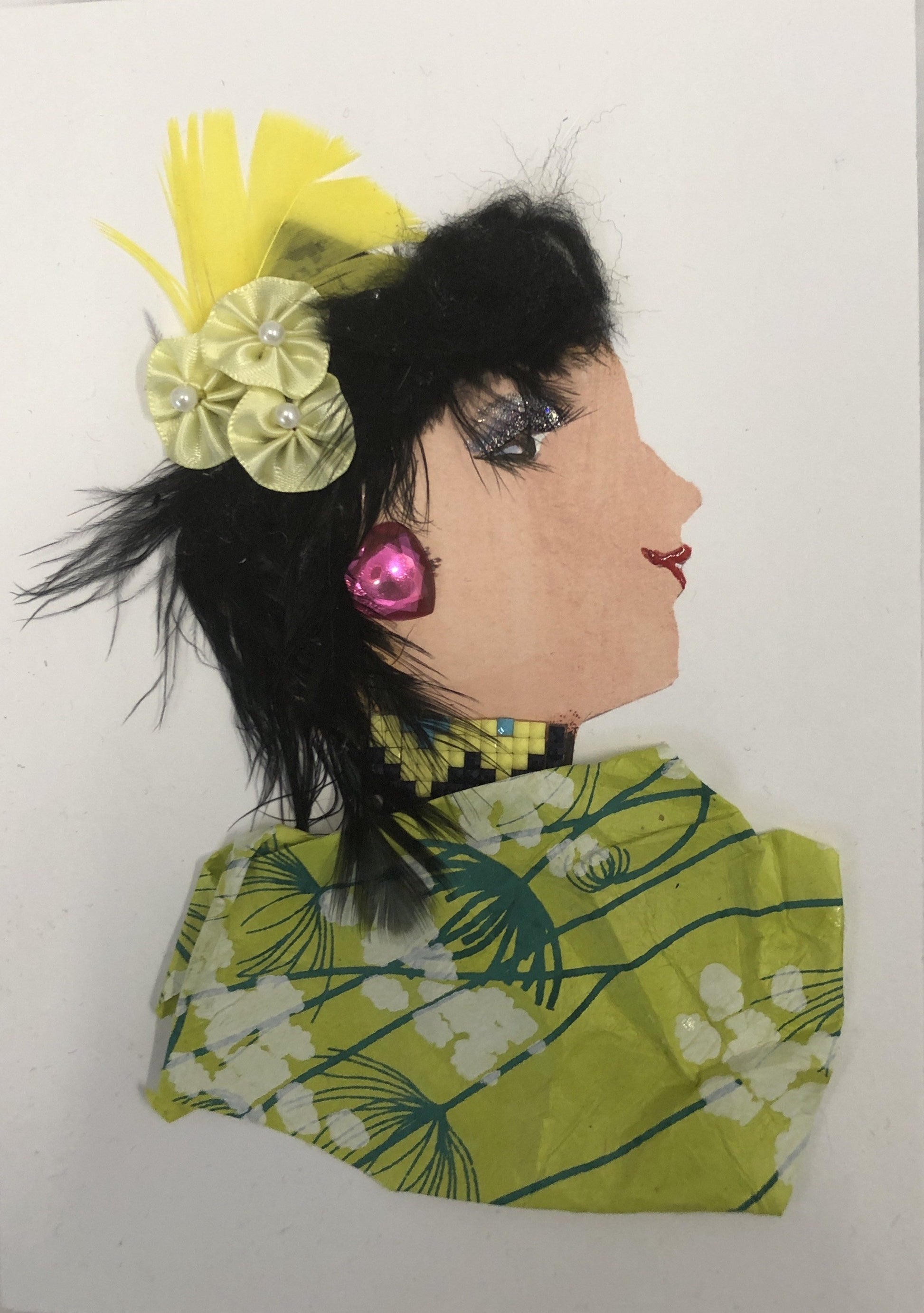 This card has been given the name Chelsea Chick. Chelsea wears a green blouse with a cherry blossom pattern on it. In her black hair she wears a yellow flower with a yellow feather behind it, and a pink heart gem earring.