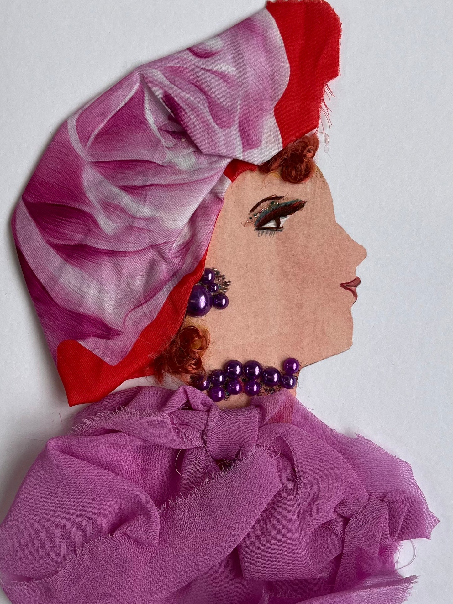 This card has been given the name Rosina. Rosina wears a chiffon pink blouse that is tied up at the top. Her jewellery is made of purple pearls, and her headscarf is a rose flower pattern, her red curly hair peeking out of it. A beautiful card  to frame for your home or the perfect gift for someone to celebrate