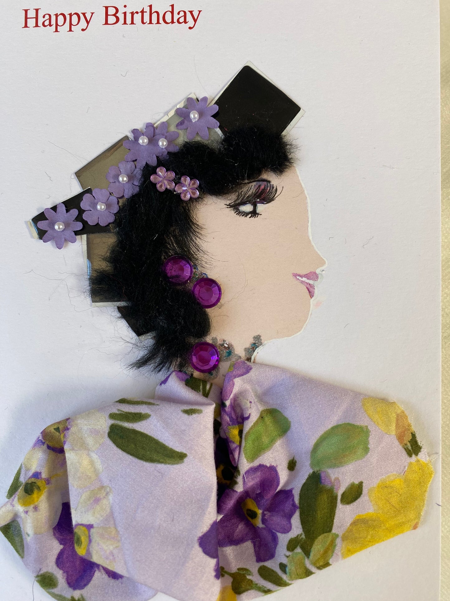 I designed this card of a woman who is wearing a charming green hat with purple flowers. She wears a beautiful floral print blouse. She wears luxurious purple jewellery. In the top corner it says happy birthday in red lettering.