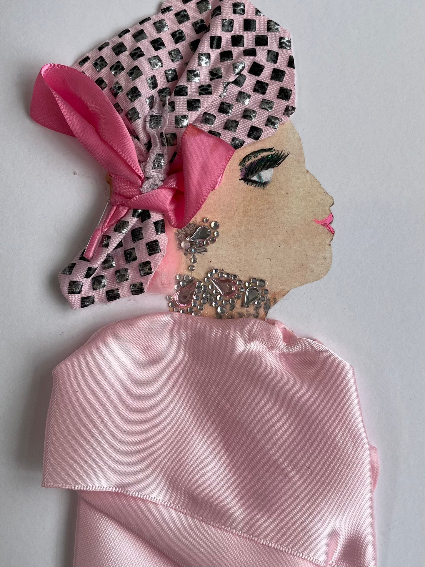 This card shows a woman wearing a baby pink silk blouse and a checkered headscarf with a pink satin bow wrapped around it.