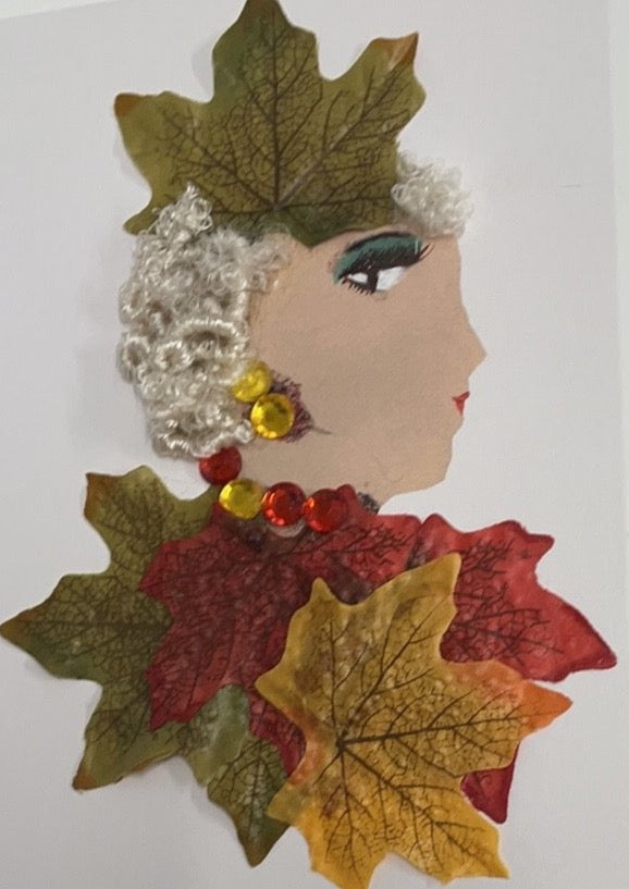 This card was given the name Cuba Cubator. Cuba wears a dress made of oak leaves. The leaves are all different colors, one green, one red, and one yellow. There is another green leaf in her platinum blonde hair. She wears a red and yellow gemstone necklace, and matching earrings.
