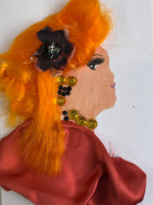 This card is called Orangina Osterley. She wears a dark orange silk blouse and her hair is a brighter orange. She wears a brown flower in her hair, and yellow jewellery. 