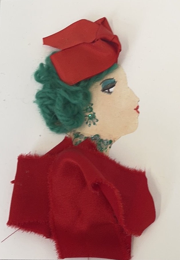 This card has been given the name Maria. Maria wears a red fabric blouse and a matching headscarf in her green yarn hair.