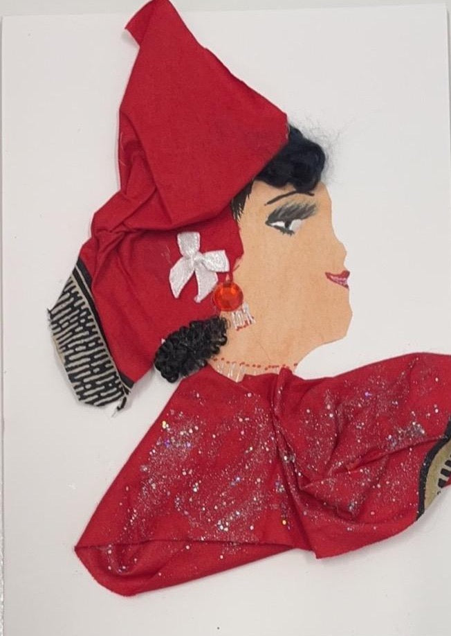 This card has been given the name Tracy. Tracy wears a matching headdress to her blouse, both of which are a red fabric with a small amount of black detailing. The blouse has a glitter overlay on the fabric. In her headdress, there is a small white bow. Her curly black hair peeks out the sides of the headdress. This is a  beautiful card  to frame or a perfect gift for someone to celebrate a birthday anniversary or just to cheer yourself up.