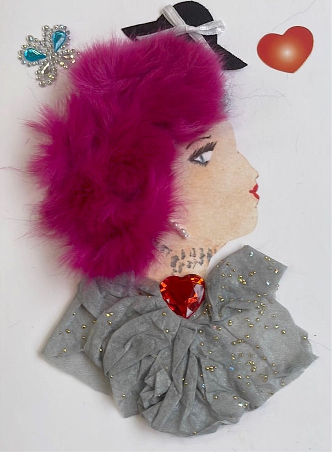 This card is called platinum pink. She wears a grey blouse, has hot pink furry hair, and behind her there is a small black hat, a red heart, and a rhinestone butterfly.