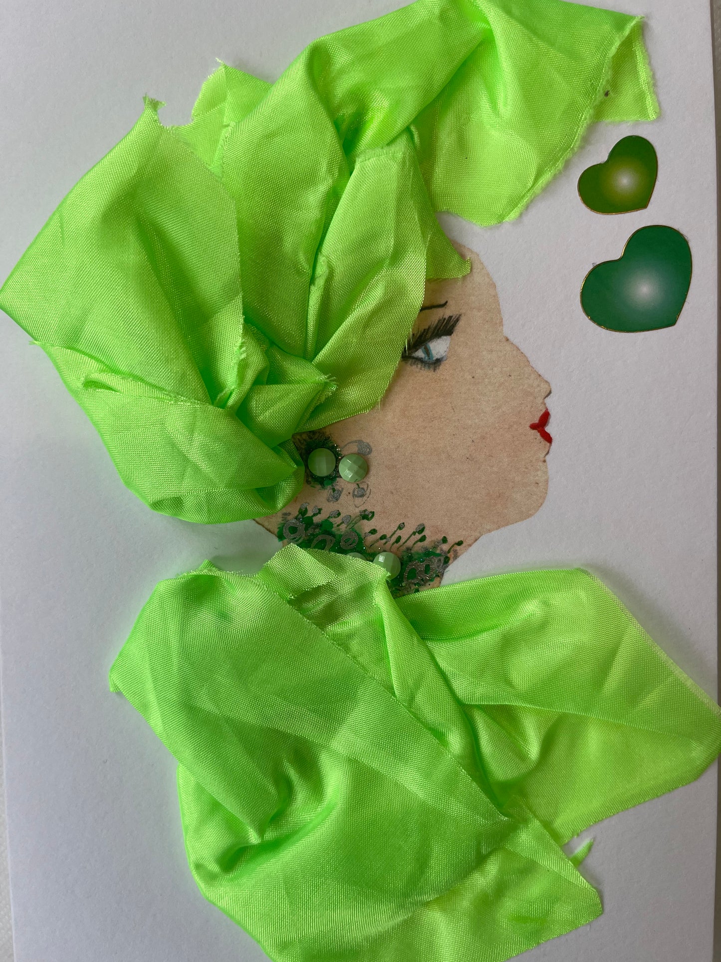 This card depicts a woman named Lucy. Lucy wears a matching blouse and headdress which are a lime green silk material. Her jewellery is green and simple. In the righthand corner, there are two hearts that are also green.