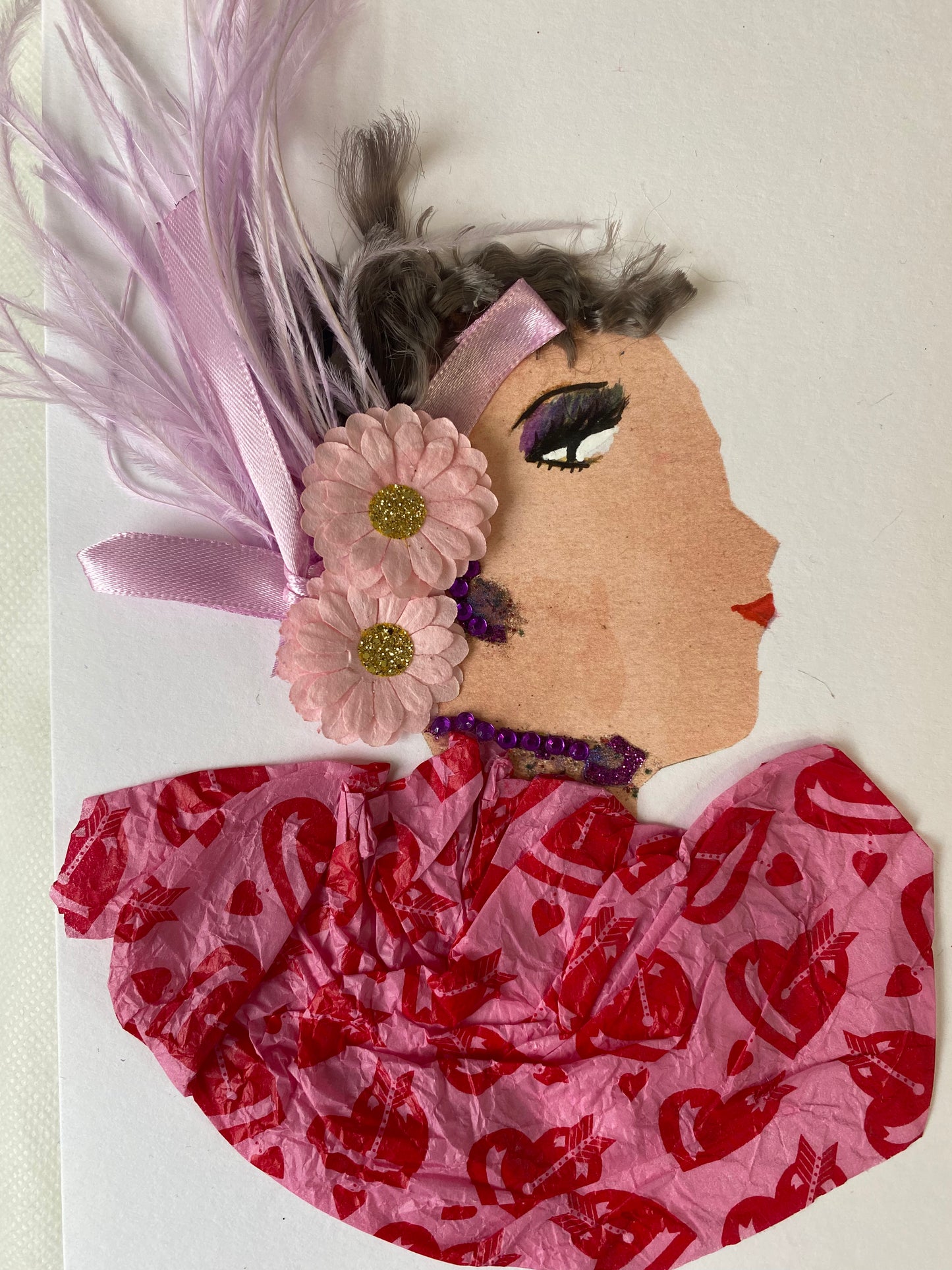 I designed this card of a woman named Carmen Cupcake. She has a white skin tone and headwrap that has two pink flowers with purple feathers. She wears a pink blouse with a red heart pattern. She wears shiny purple jewellery.