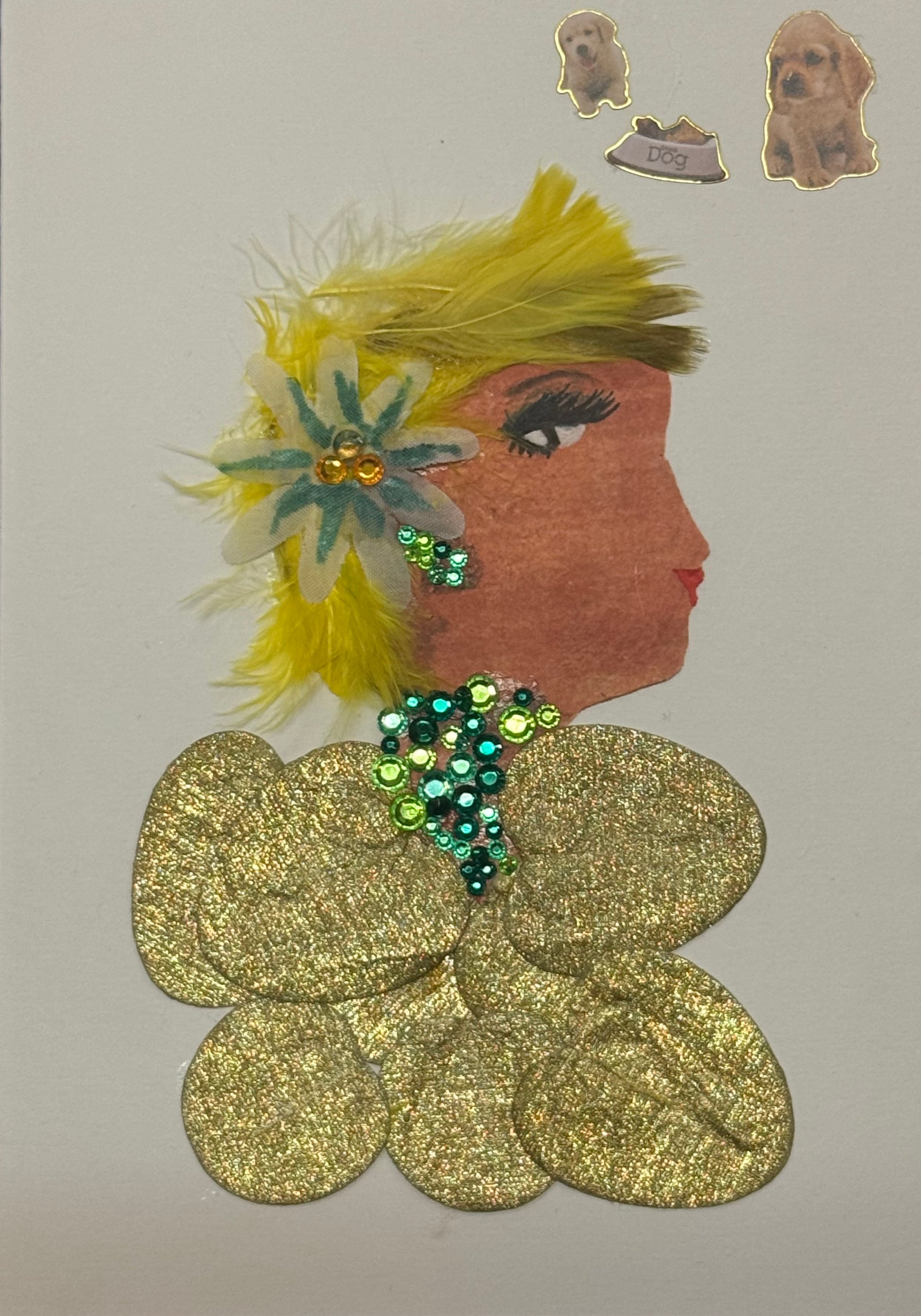 Handmade greeting card that doubles as a piece of art featuring a side-profile silhouette of a woman with a warm complexion. Her hair is styled with bright yellow feathers that fan outward, creating a soft, textured halo around her head, accented by a multicolored floral embellishment placed near her ear. She wears green gem jewellery for neckalce and earrings. Her top is glittery gold,  that is made up of circle shapes. Placed in the top right corner is three dog stickers above her head that add character.