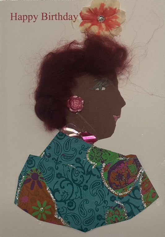 Handmade birthday card that can double as a piece of art featuring a woman with textured burgundy hair and a flower accessory above her head. She wears a colorful patterned outfit with decorative jewels, and the words “Happy Birthday” appear above the design.