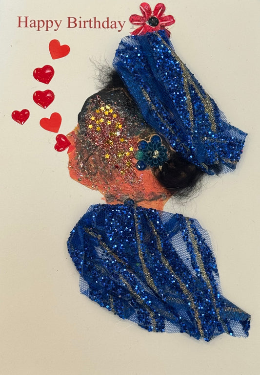 Handmade collage greeting card depicting a right-facing side profile of a dark-skinned woman with voluminous, textured black hair styled outward in a natural shape. Her face includes defined eyelashes, a shaped eyebrow, and soft pink lips. She wears large, bright turquoise-blue beaded earrings and a matching clustered statement necklace made of round, reflective beads. Her clothing is made from blue fabric featuring a floral print with pink flowers and green leaves. The background  says “Happy Birthday" 