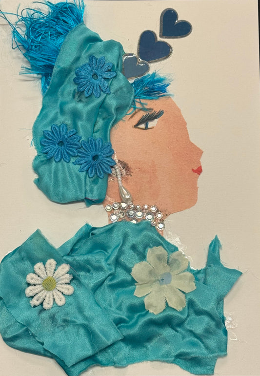 
Handmade greeting card that can double as art. Side-profile portrait of a woman facing right, with fair skin and a teal-blue headwrap adorned with fabric flowers. Her outfit is made of soft blue fabric with white and light blue floral appliqués. She wears a dangling, pearl-like earring and decorative rhinestones. Two blue heart shapes float above her head. Her eye is delicately drawn, and her lips are red. The textures are soft and flowing, with fabric folds and floral details giving a gentle, airy feel.