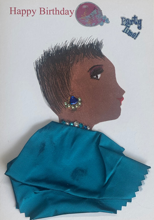 A handmade birthday card featuring a side-profile illustration of a woman with a short textured haircut. She wears blue gem earrings and a teal satin fabric garment forming her shoulders. Small gem accents appear along her neckline. The background is white with “Happy Birthday” printed above and small decorative stickers.