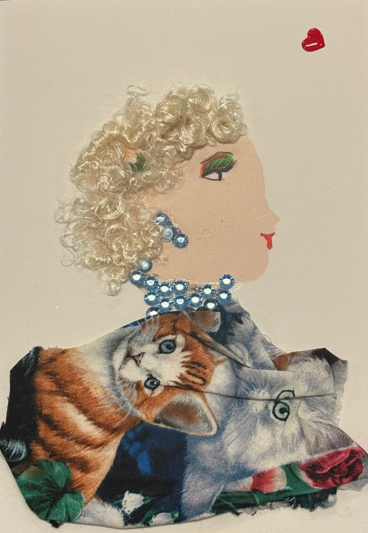 A side-profile collage portrait of a woman facing right, with light skin and short, tightly curled blonde hair made from textured fibers. A small floral detail is tucked into her hair. She wears blue gem-like earrings and a matching necklace composed of clustered circular embellishments. Her clothing features a printed fabric with detailed images of cats, adding a whimsical and playful element. Her eye makeup includes green tones, and her lips are red. 