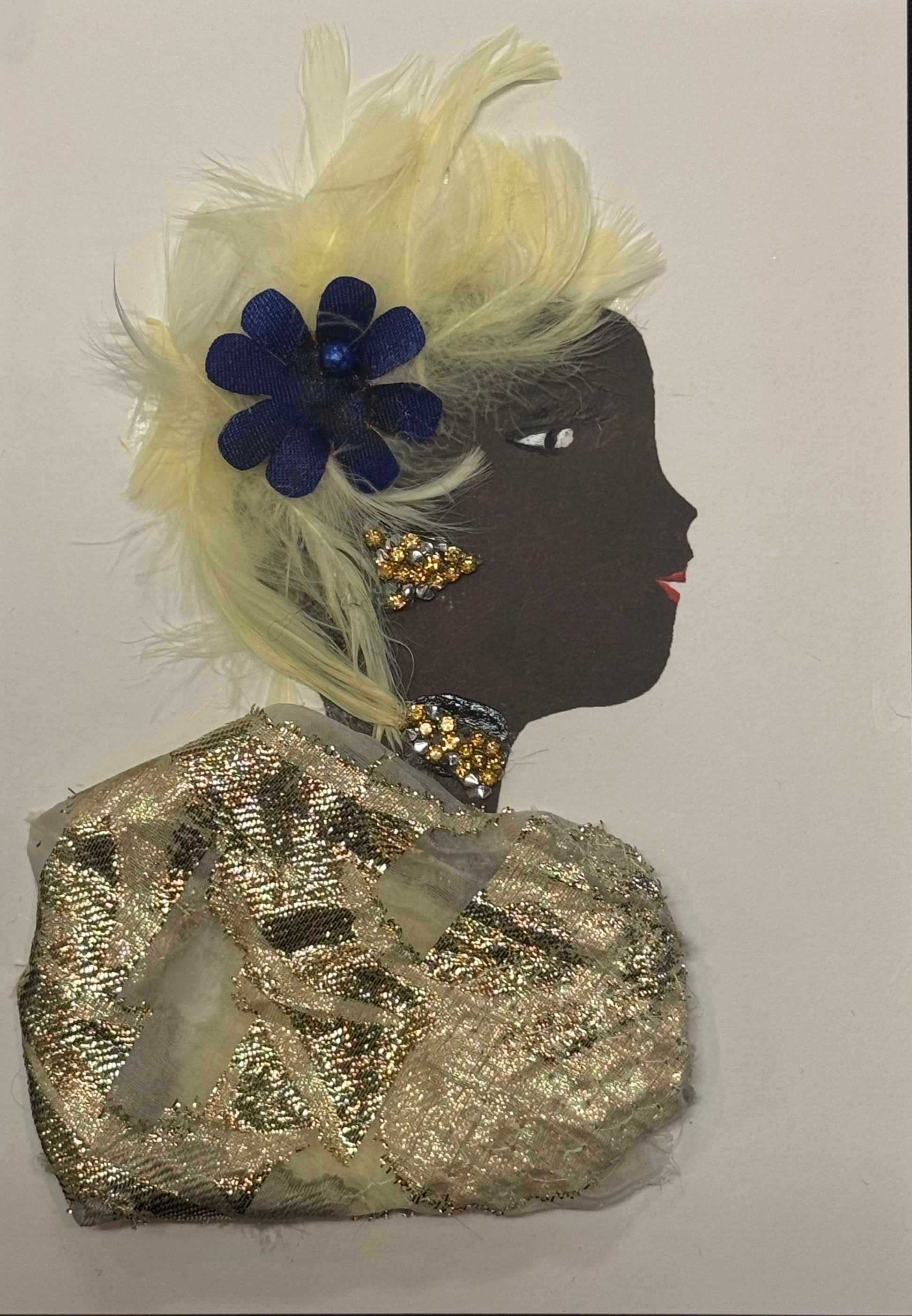 Handmade greeting card that can double as a piece of art featuring a dark brown silhouette of a woman in profile, styled with soft cream-colored feathers forming her hair or headpiece. A deep navy blue flower sits within the feathers, adding contrast. She wears gold-toned textured fabric as clothing and has gold embellishments for earrings and a necklace. Her facial details include a defined eye with lashes and red lips, all layered on a white background with mixed materials including feathers and fabric. 