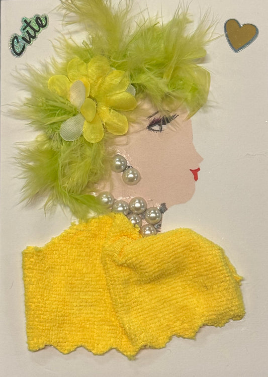 Handmade greeting card that can double as a piece of art, featuring a side-profile silhouette of a woman with light skin tone, decorated with lime green feathers and a layered yellow fabric flower in her hair, wearing pearl earrings and a chunky pearl necklace, with a textured yellow fabric forming her top, all set against a clean white background.
