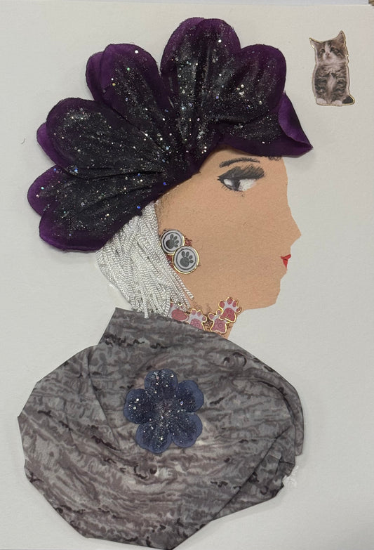 Handmade greeting card that can double as a piece of art, featuring a woman in profile with a large dark purple glittered floral headpiece. She wears a textured grey garment with a blue flower embellishment and delicate jewelry accents. Above, there is also a detailed sticker of a grey cat in the top right corner above her head. 
