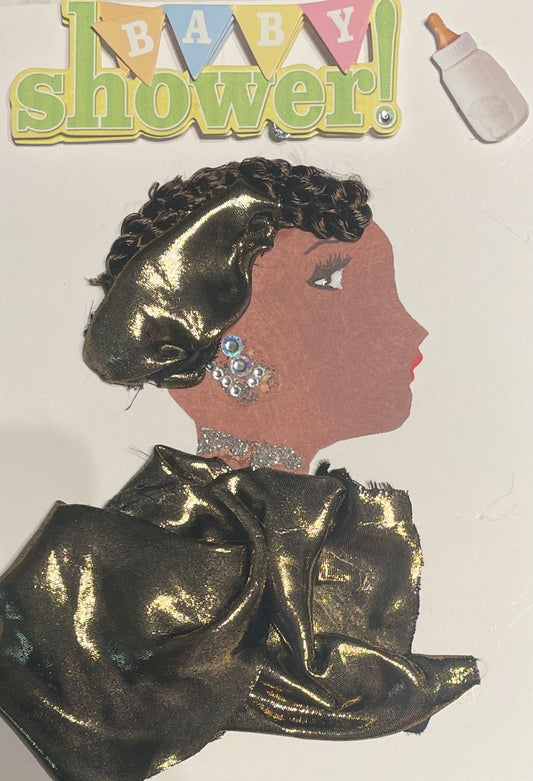 This card depicts a woman who is wearing a golden blouse and matching hat. She also wears silver earrings and a glittery necklace. On the top of the card there is a sticker that says "Baby Shower!' next to that sticker is sticker of a baby bottle.