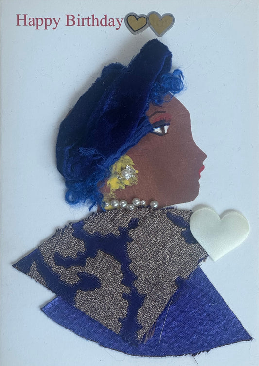 A handmade birthday card featuring a side-profile illustration of a woman wearing a royal blue fabric hat. She has pearl necklace details and yellow gem earrings. Her outfit is made from layered blue and neutral patterned fabric. Her lips are red and her eye is delicately illustrated. The background is white with two heart stickers above.