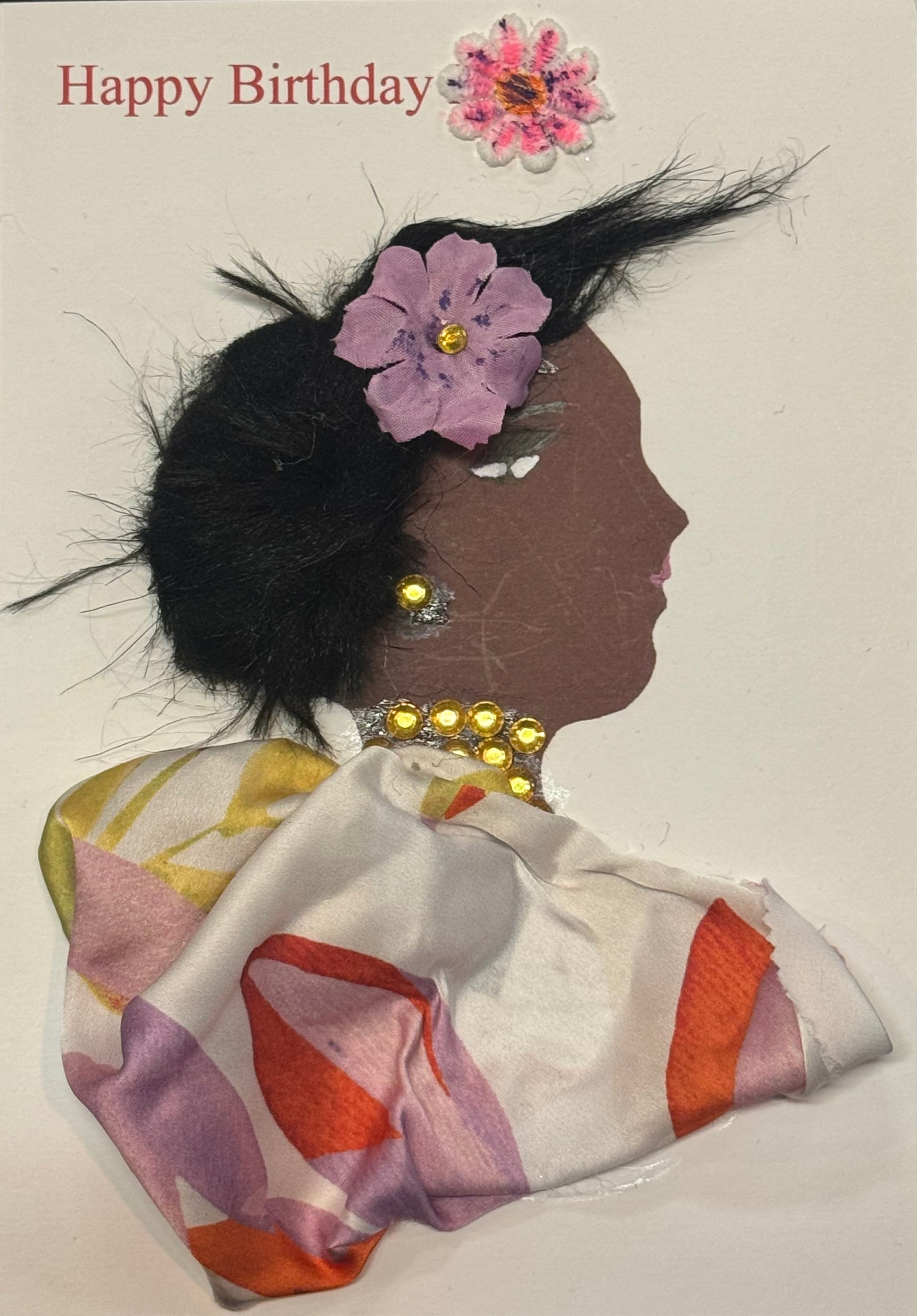 Handmade greeting card that can double as a piece of art, featuring a dark-skinned silhouette with textured black hair styled outward, adorned with a purple flower and gold gem jewelry, wearing a multicolored patterned fabric top, with “Happy Birthday” text above on a white background with a pink and purple flower next to the text above her head.