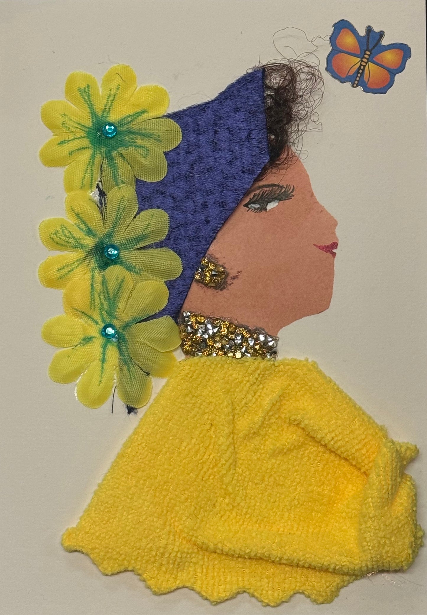 Handmade greeting card that can double as a piece of art featuring a side-profile silhouette of a woman with a warm tan complexion wearing a textured yellow sweater and a deep purple headwrap. Bright yellow flower embellishments with green details line the side of her head, accented with small blue gem centers. She wears gold glitter earrings and a matching necklace. A small colorful butterfly appears near her head, and her facial features include detailed lashes and red lips, all on a white background.