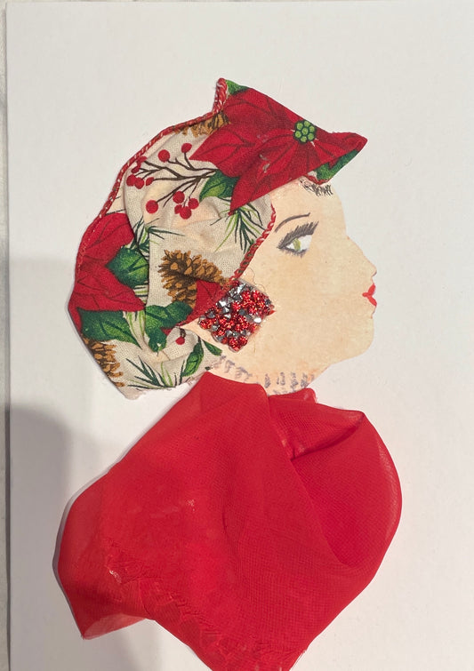 Handmade card featuring the side profile of a woman with painted facial features and red lipstick. She wears a festive fabric headwrap adorned with poinsettias, pinecones, and holly. Her outfit is made from red mesh fabric, and her earring is crafted from red and silver glitter. The background is plain white.