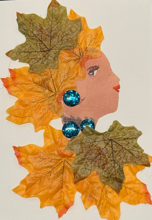 Handmade greeting card that can double as a piece of art featuring a side profile collage of a woman surrounded by layered autumn leaves in orange, yellow, and brown tones forming her hair and clothing. She wears large bright blue gem earrings, creating contrast against the warm palette.