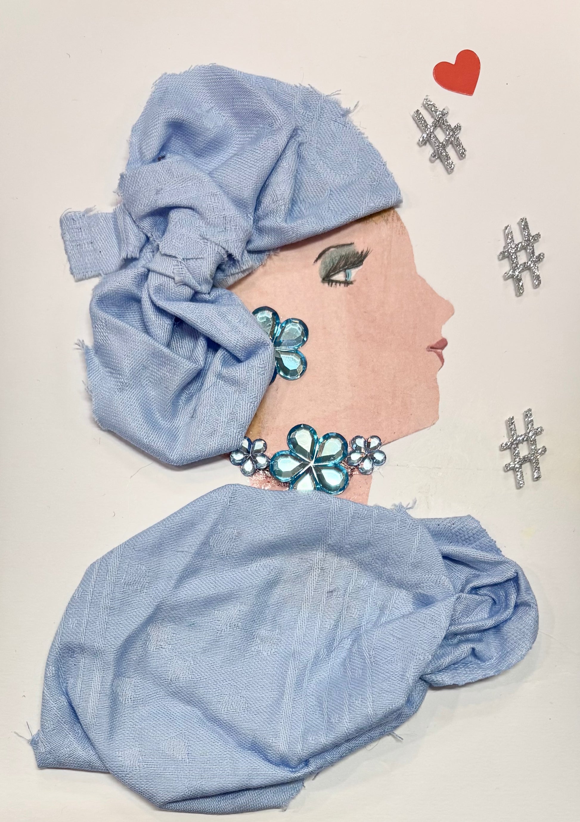 A woman wears a matching baby blue headwrap and blouse. Her jewellery is made of blue gems that resemble flowers. A little red heart sits at the top right of the card with three silver hashtags scattered below. 