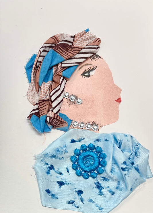 A woman wears a multicoloured headwrap with blue, brown, and white. Her blouse is a baby blue with darker blue splotches and a blue flower in the center. She has sparkling silver earring and matching necklace. 