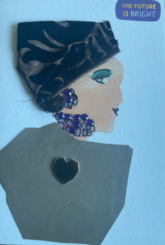 This is a handmade card of a woman named Brown Pudding. She wears a shiny dark brown head wrap with a leaf-like pattern and has green eye shadow. Her earrings and necklace are made of sparkly purple gems. Her outfit is made of soft brown leather-like fabric, decorated with a black heart-shaped badge. The corner of the card says, "The future is bright."