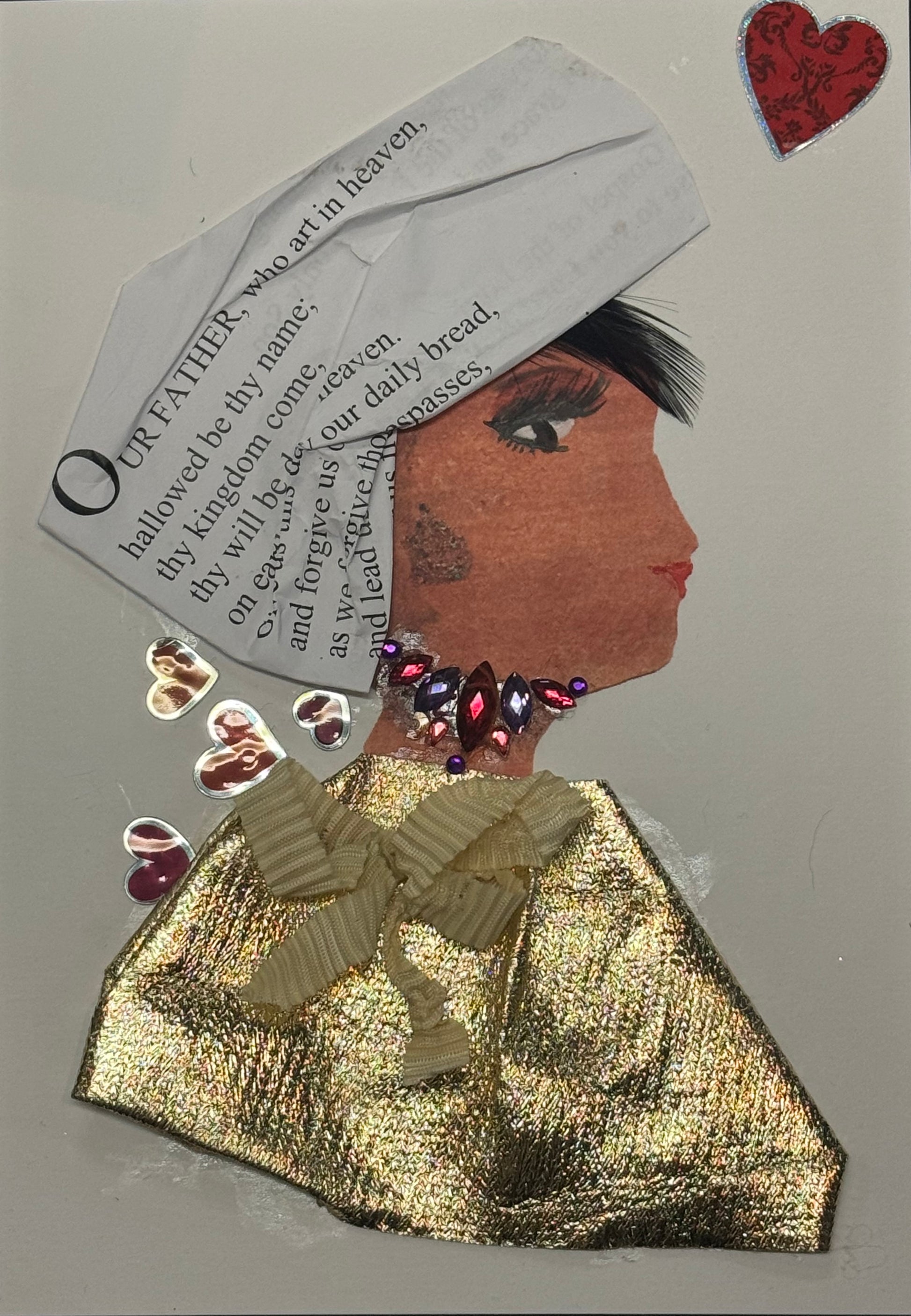 Handmade greeting card that can double as a piece of art featuring a side-profile portrait of a woman with a headpiece made from cut paper text, a deep brown textured face, and a gold metallic fabric outfit with a sculpted bow detail. The design includes rhinestone embellishments around the neck and small heart accents, combining collage techniques with layered textures for a bold and expressive visual composition.