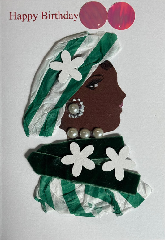A handmade birthday card showing a woman in side profile with dark brown skin facing right. She wears a green and white striped headwrap made from layered textured material with a white flower shape attached. Her jewelry includes pearl earrings and a row of pearl beads around her neck. A deep green velvet band with two white flower cutouts sits across her shoulders, layered over more green-and-white striped material. Two red circular stickers appear near the top beside the red “Happy Birthday” text. 
