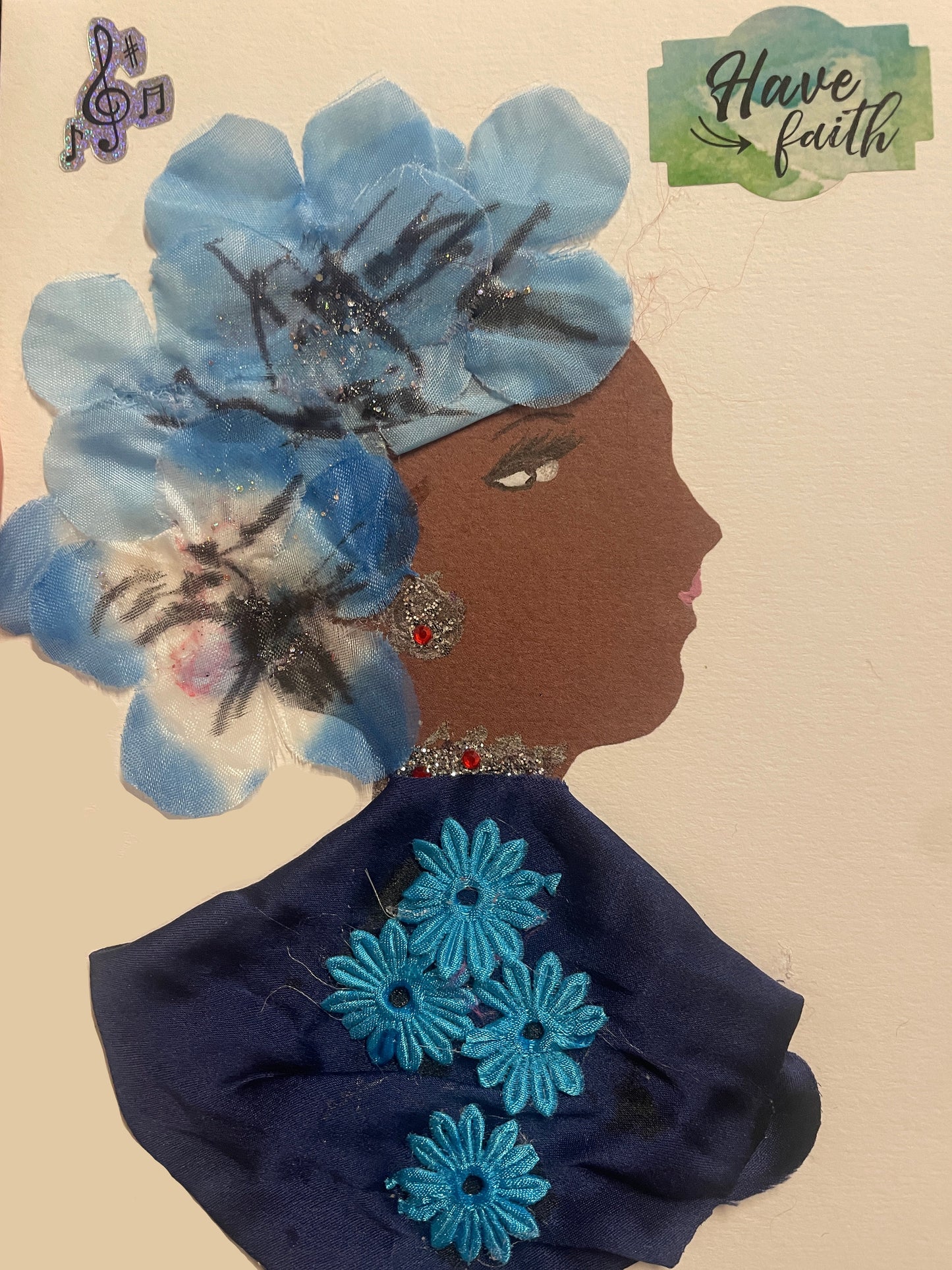 This is a handmade card of a woman named Canada Water Kaitie. She wears a large floral crown in blue, a deep blue shawl with sewn flowers, and sparkling earrings. Stickers say “Have faith” and show musical notes.