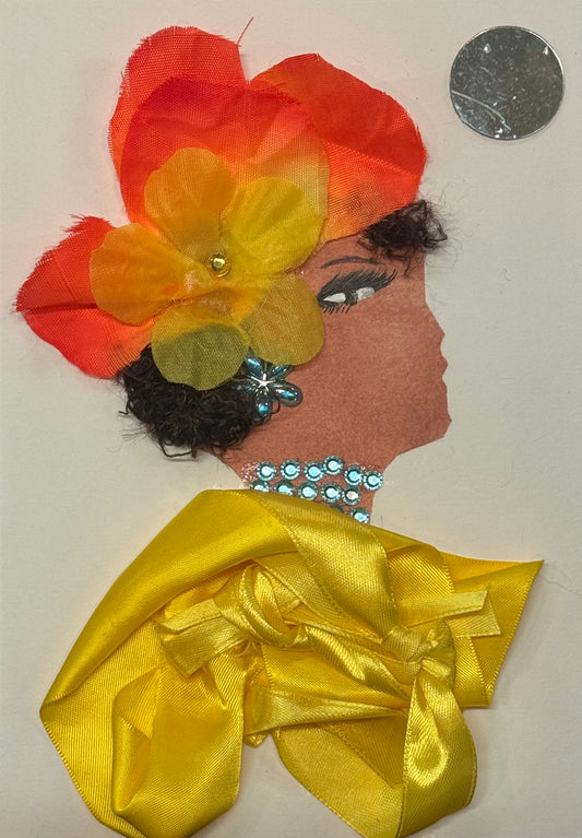 Handmade greeting card that can double as a piece of art, featuring a side-profile silhouette with curly dark hair, adorned with a large layered orange and yellow fabric flower that is ombre coloured with orange and yellow and has a small yellow gem in the centre. She also wears blue gem earrings and necklace. For her shawll she wears a bright yellow satin top that has a bow garment in the middle. Above her head on the right, the is a circular reflective gem that acts as a mini mirror. 