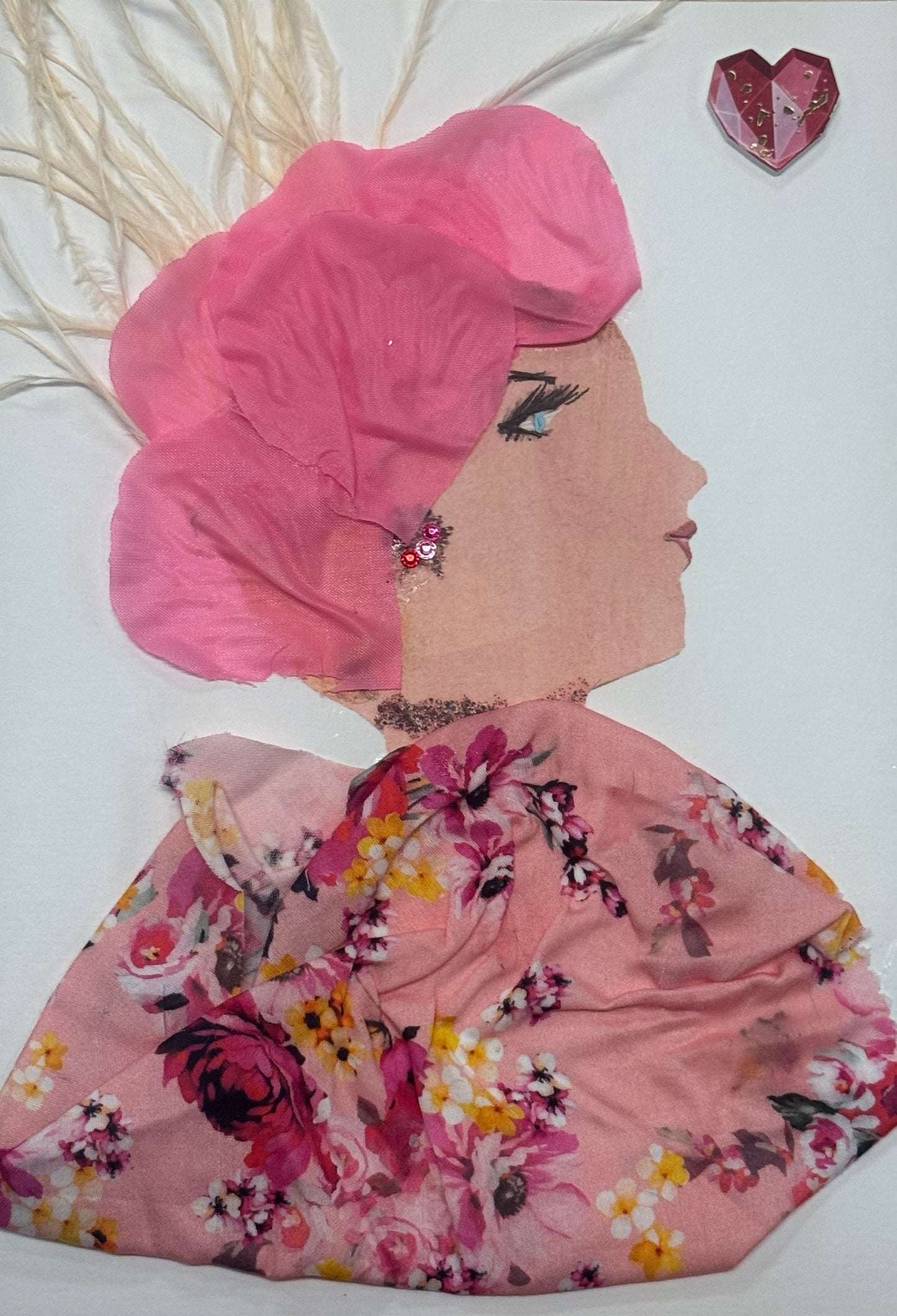 Handmade greeting card that can double as a piece of art, depicting a side-profile of a woman wearing a soft pink petal-like head covering. She is dressed in a flowing floral-patterned fabric with shades of pink, yellow, and green. Light feather accents extend from the top, adding texture and dimension. Her features include a gentle gaze with light blue eye detail and soft makeup.
