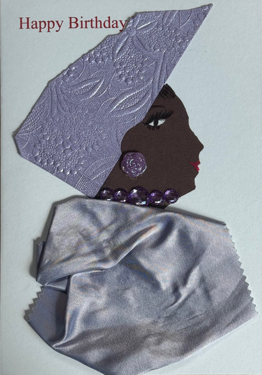 A handmade birthday card showing a side-profile portrait of a woman with deep brown skin facing right. She wears a textured lavender embossed headwrap folded into a structured angular shape. A round purple gem earring sits on her ear, and a chunky necklace made of translucent purple beads circles her neck. Her wrap is made from shiny silver satin fabric draped across her shoulders. She has long painted eyelashes and red lips. The background is white with “Happy Birthday” printed in red at the top.