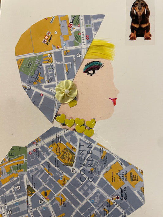 This is a handmade card of a woman named Evie Mapmaker wearing an outfit made of map paper and adorned with yellow hearts and a yellow satin flower, next to a dog sticker.