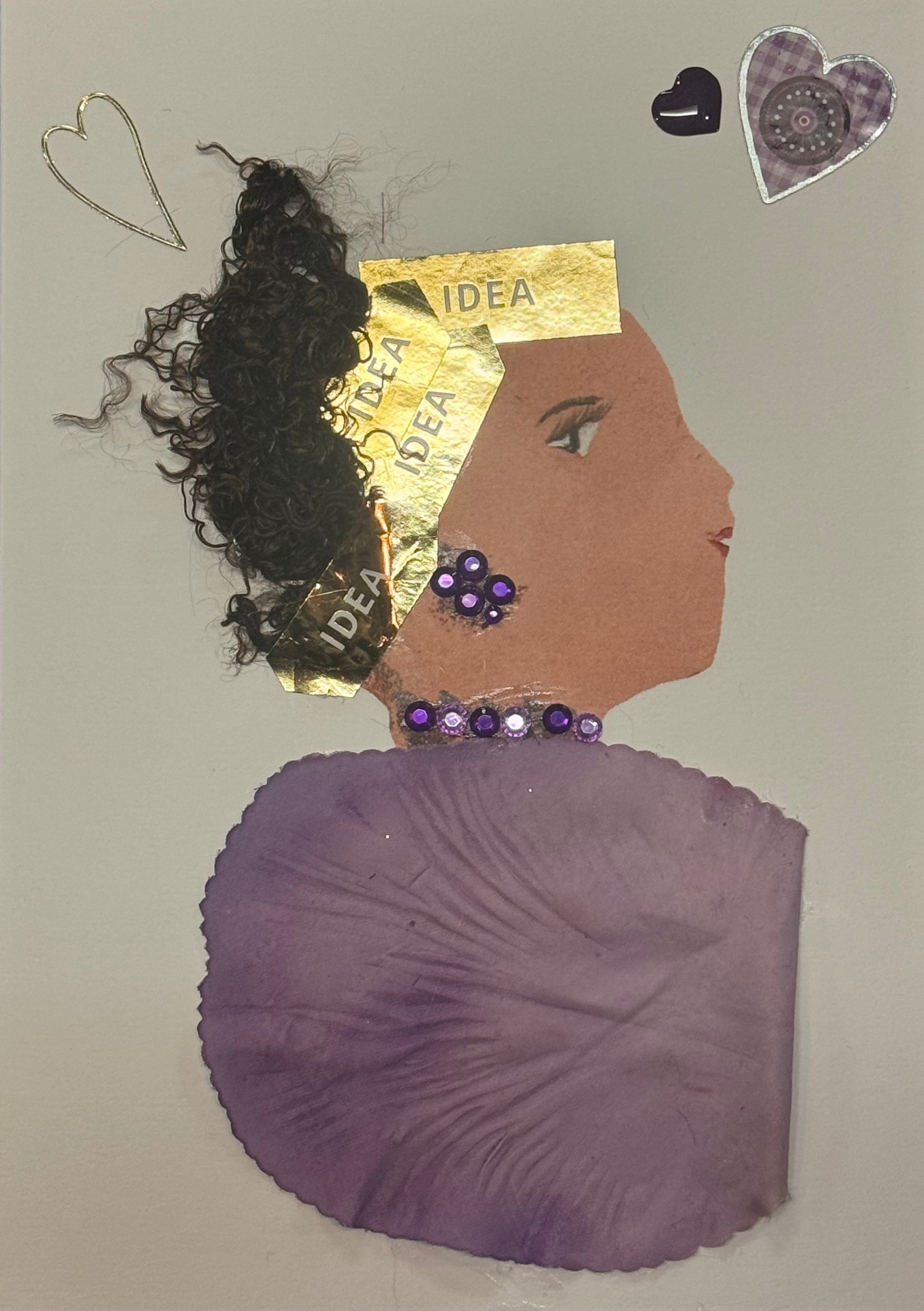 Handmade greeting card that doubles as a piece of art featuring a side-profile silhouette of a woman with curly dark hair partially wrapped in a gold headwrap labeled “IDEA.” The headwrap sits across the top of her head, with the metallic gold tone creating a strong focal point against the darker hair. She wears purple gem jewelry that adds a bright pop of color and draws attention to her ear and neckline. Her top is made from soft purple textured fabric in the shape of a flower petal.