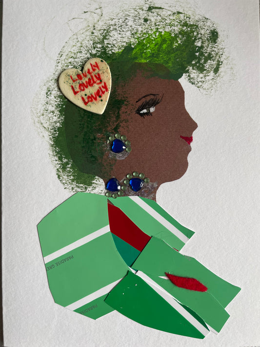 This card depicts a woman with green hair and a white heart that says ‘lovely’ pinned in her hair. She wears a green blouse with red and white stripes. She also wears blue and green jewellery.