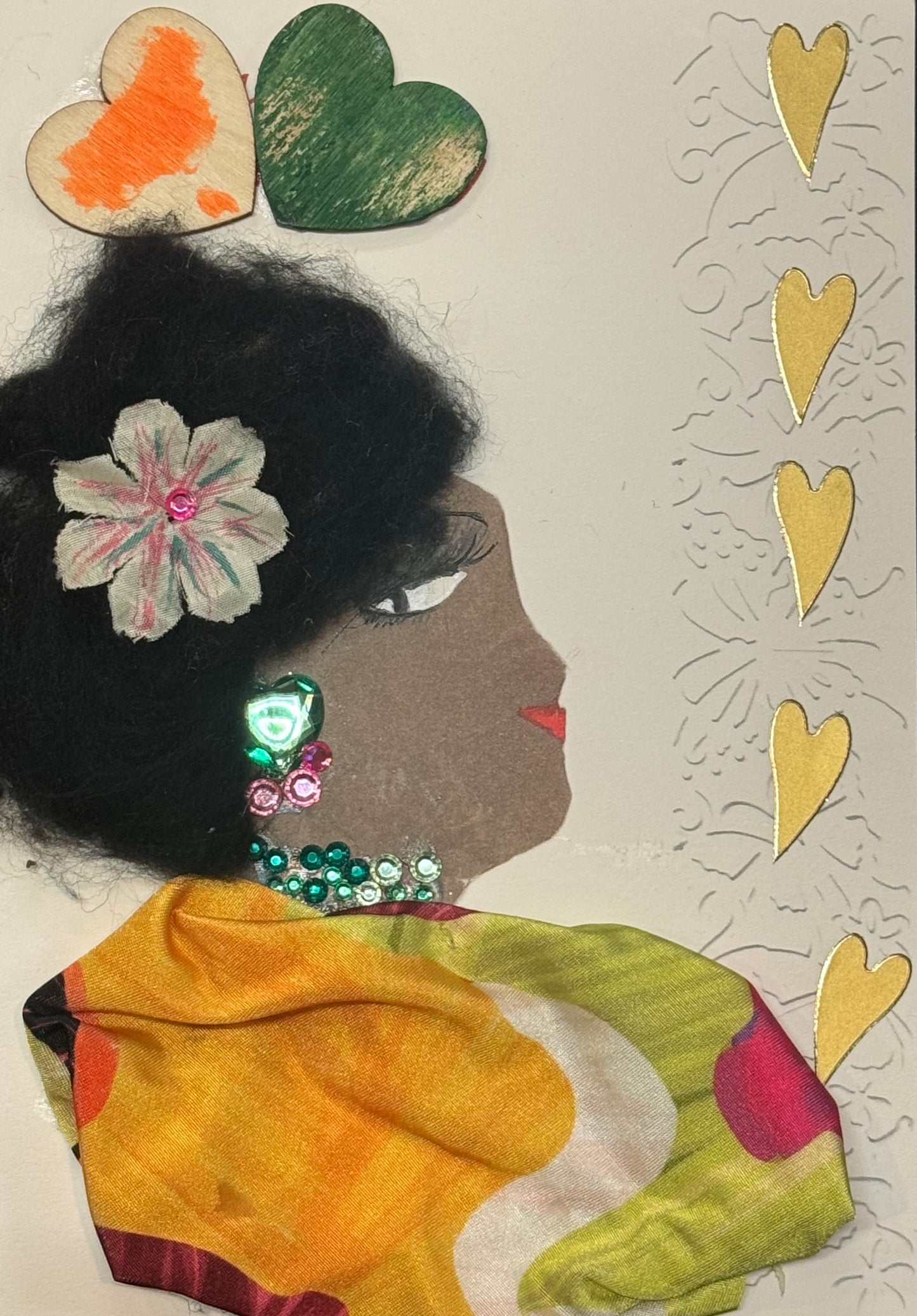 Handmade greeting card that doubles as a piece of art featuring a dark-skinned side-profile silhouette with textured black hair shaped upward and outward. A small floral hairpiece is tucked into the hair, adding a delicate decorative focal point near the crown. She wears colorful green and pink gem earrings with a matching necklace, which stand out brightly against her complexion and draw attention to the face and neckline. A vibrant patterned fabric wrap forms her clothing, with layered colors and textures