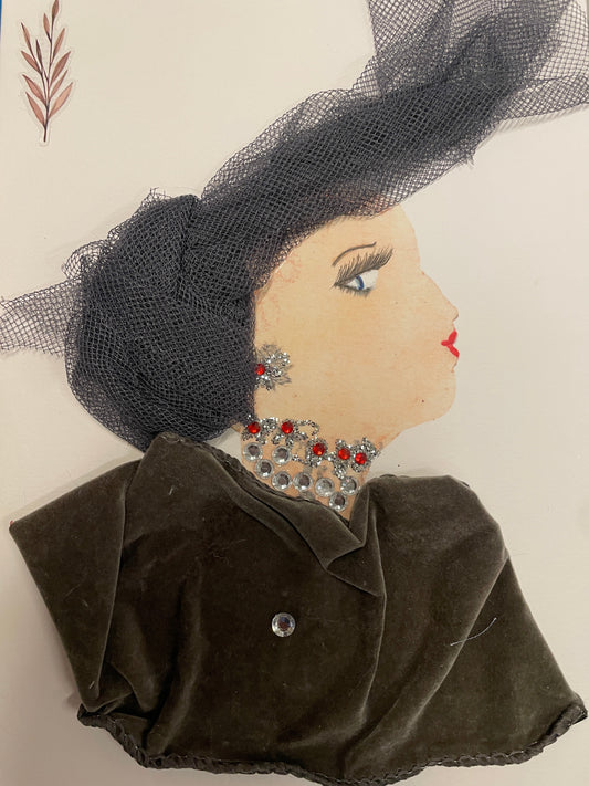 Handmade card of a woman in profile wearing a sculptural black mesh headwrap and silver-red gem earrings. Her black velvet dress is accented with a single rhinestone. Her neckline is decorated with layered silver and red gems. A soft leaf sticker is in the top left corner.