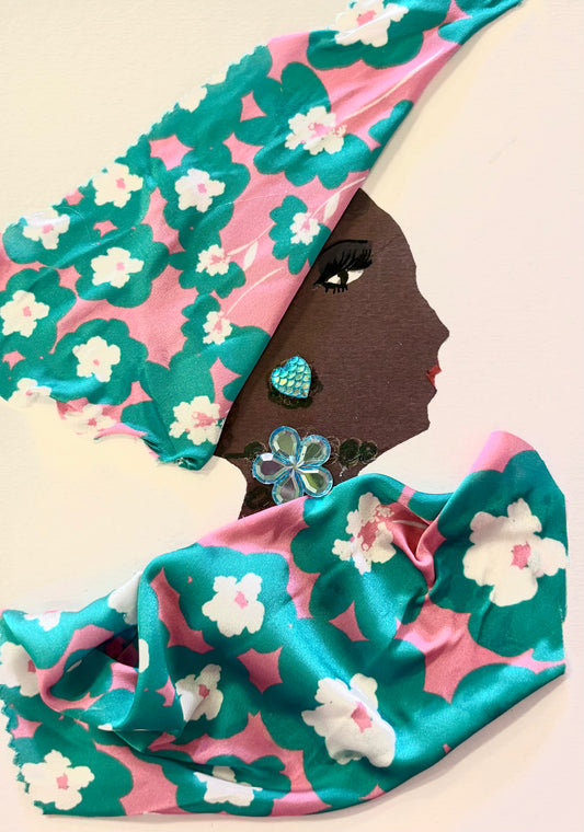 Handmade portrait of a woman in profile, created with mixed media. The woman has deep brown skin and is wearing a vibrant headwrap and garment made from pink fabric with bold teal and white floral patterns. Her face features defined eyelashes, red lips, and a turquoise heart-shaped earring. She also wears a light blue beaded flower necklace. The artwork combines fabric, sequins, and painted elements for a textured, three-dimensional look.