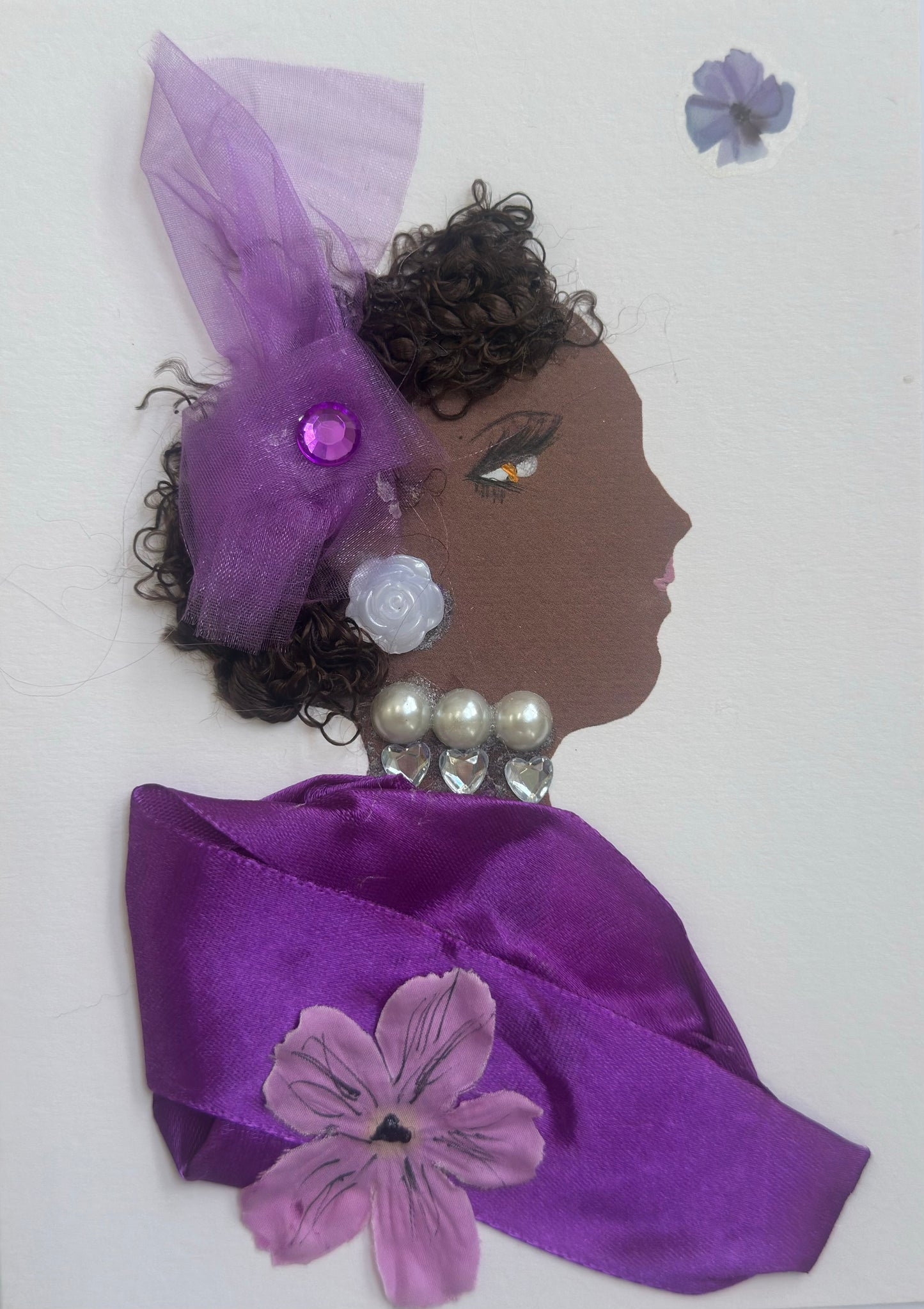A handmade portrait of “Taplow Tess,” featuring curly dark hair, a purple tulle headpiece with a gemstone, white floral earring, pearl-and-heart necklace, and a violet satin wrap decorated with a fabric flower.