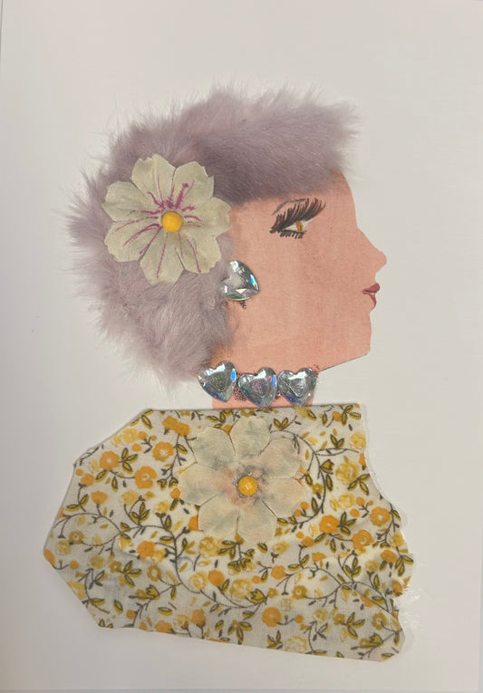 A handmade card shows a side-profile portrait of a woman with pale skin, soft lavender fluffy hair, and pink lips. She has a cream flower in her hair, iridescent heart-shaped earrings, and a silver heart choker. Her dress is made of yellow floral fabric with a matching flower embellishment in the center.