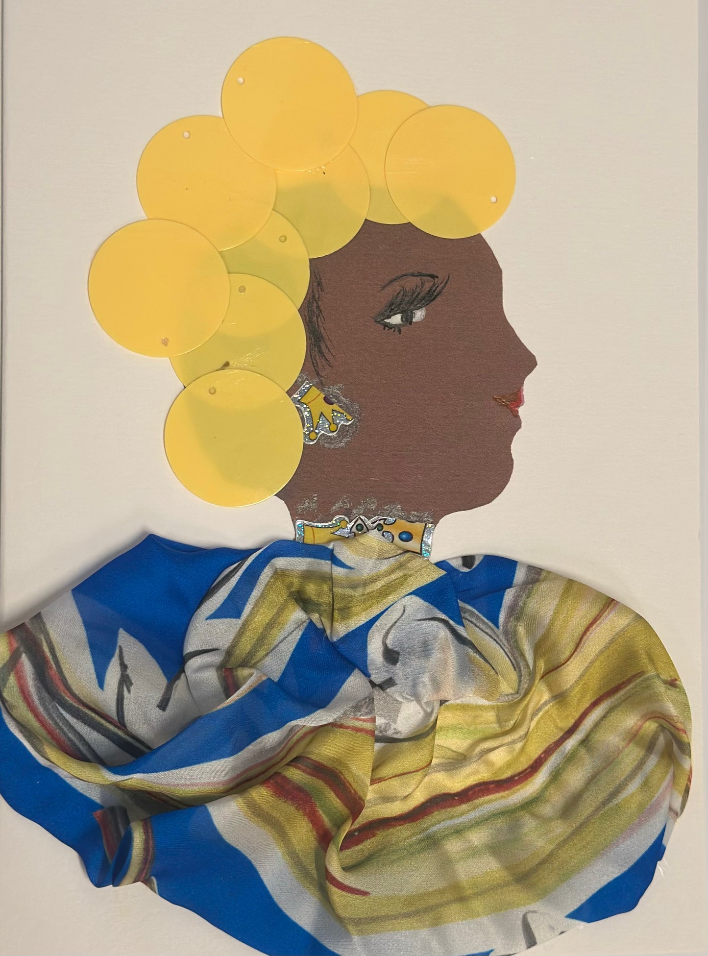 A handmade card displays a side-profile portrait of a woman with deep brown skin, long eyelashes, and pink lips. She has large yellow circular discs arranged around her head like stylized flowers, wears patterned yellow-and-silver earrings, and is draped in a blue, gold, and white patterned scarf. The overall design is bright, cheerful, and spring-inspired.