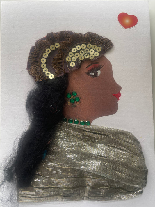 This is a handmade card of a woman named Gilda Goldhawk. She wears a metallic gold blouse, has long black hair with a sequinned headpiece, green gem jewellery, and a red-orange heart sticker.
