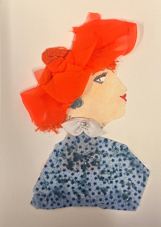 A handmade collage card featuring a woman in profile with a vibrant orange textured headwrap and orange hair. She wears bold red lipstick, sparkly blue earrings, and a white bow at her collar, paired with a blue floral-patterned blouse. The design uses layered fabrics and embellishments and sits on a plain white background.